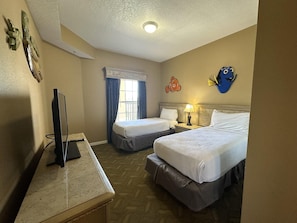 A hotel room with two beds, a desk with a television, a window with curtains, and wall decorations including a fish. - 2403 Spacious 2/2 Resort Condo Near Disney (Orlando)