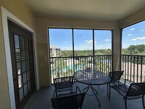 A balcony with a round table and four chairs, overlooking a swimming pool and buildings. - 2403 Spacious 2/2 Resort Condo Near Disney (Orlando)