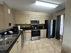 A compact kitchen with a microwave, stove, refrigerator, and a sink. - 3203 Spacious 2/2 Resort Condo Near Disney (Orlando)