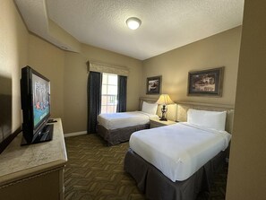 Ein Hotelzimmer mit zwei Betten, einem Fernseher, einer Lampe und zwei gerahmten Bildern an der Wand.