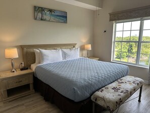 Ein Schlafzimmer mit Bett, Nachttischlampen, einem Nachttisch, einer Bank, einem Gemälde und einem Fenster mit Blick.