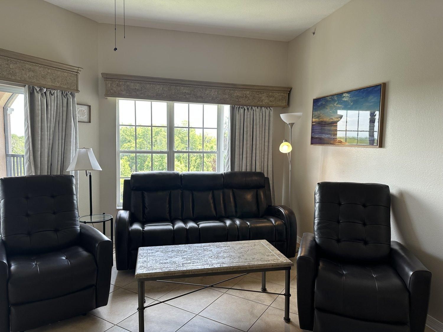 Un salon avec un canapé en cuir noir, deux fauteuils, une petite table et un lampadaire.
