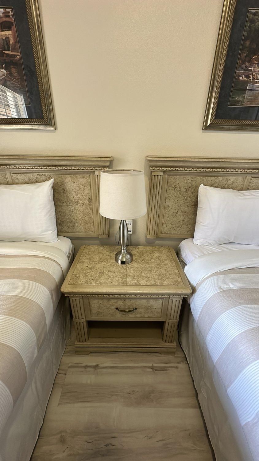Une chambre d’hôtel avec deux lits, une table de chevet avec une lampe et un tableau encadré au-dessus de chaque lit.