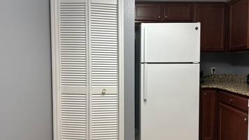 Une cuisine avec un réfrigérateur blanc, des armoires en bois et une porte blanche fermée dotée de stores horizontaux.