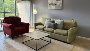 Un salon avec un fauteuil rouge, un canapé vert orné de coussins à motifs, une table basse et un lampadaire.