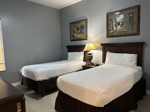 Ein Hotelzimmer mit zwei Betten, einem Nachttisch mit Lampe sowie zwei gerahmten Bildern an der Wand.