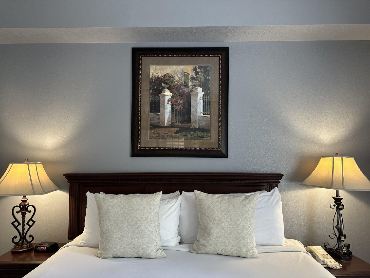Une chambre d’hôtel avec un lit, deux lampes de chevet, une horloge et une œuvre d’art encadrée au mur.