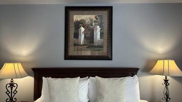 Une chambre d’hôtel avec un lit, deux lampes de chevet, une horloge et une œuvre d’art encadrée au mur.