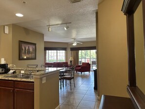 A hotel room with a kitchen area, a dining area with red chairs, and a large window providing natural light. - 4106 Spacious 2/2 Resort Condo Near Disney (Orlando)