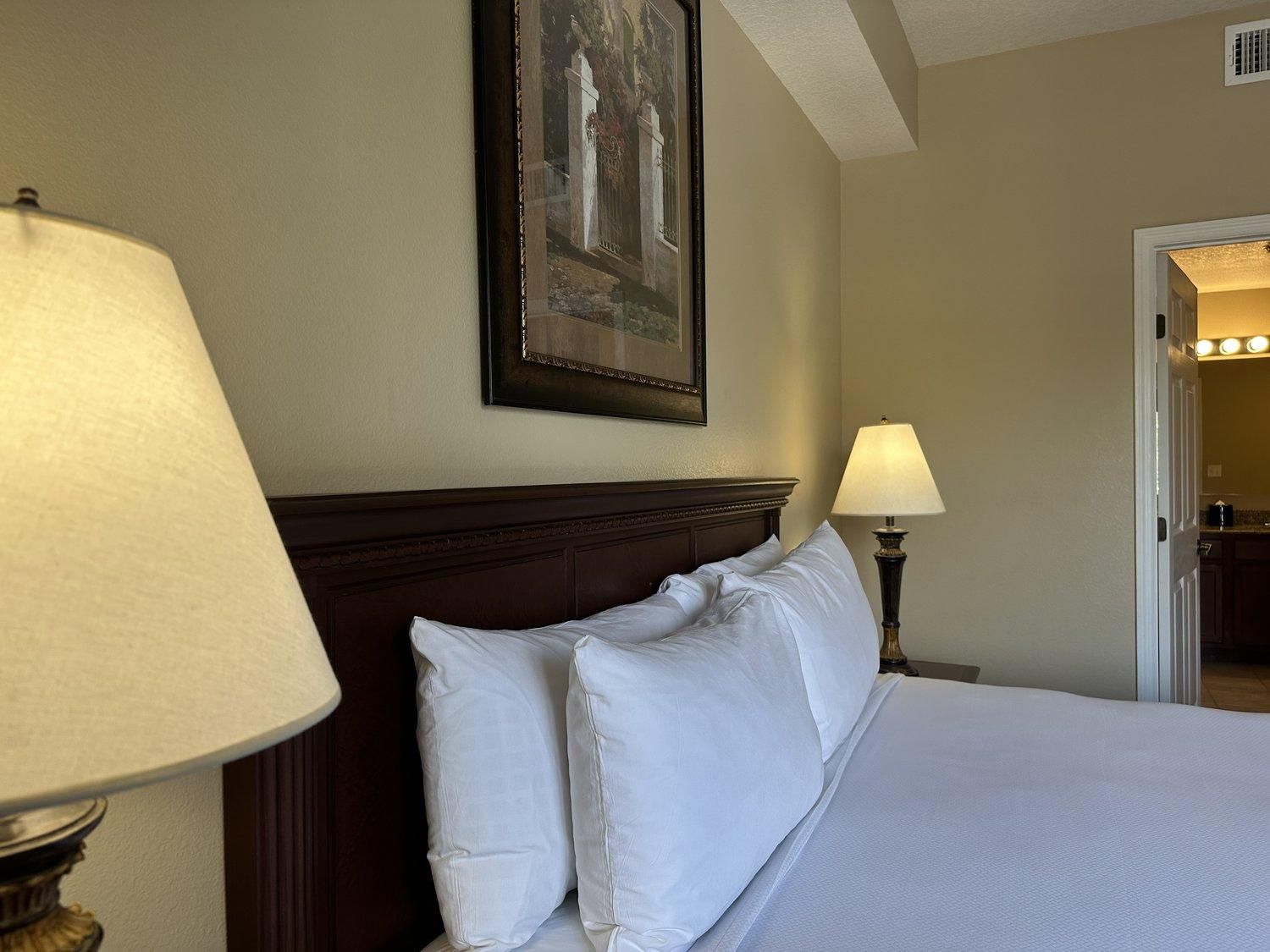 Une chambre d’hôtel avec un lit, deux lampes de chevet, un tableau encadré au mur et une porte donnant sur une salle de bain.