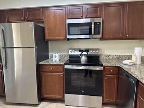 A kitchen with stainless steel appliances, wooden cabinets, granite countertops, and a dishwasher. - 4306 Spacious 2/2 Resort Condo Near Disney (Orlando)