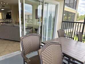A balcony with a dining table and chairs, a sofa, and a sliding glass door leading to an outdoor area.