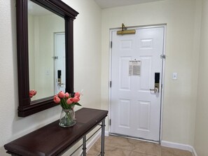 A hallway with a white door, a dark wooden console table, and a vase with pink flowers.