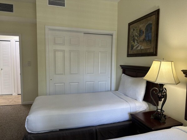 A hotel room with a bed, a nightstand with a lamp, a door, and a painting on the wall.