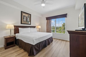 Une chambre d’hôtel avec un grand lit, deux lampes de chevet, un ventilateur de plafond, une fenêtre avec des rideaux et un tableau au mur.