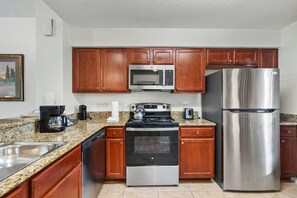 A kitchen with wooden cabinets, a stainless steel refrigerator, a microwave, a stove, and a dishwasher. - 4403 Spacious 2/2 Resort Condo Near Disney (Orlando)