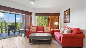 Un salon avec un ensemble de canapés rouges, une table basse et un ventilateur de plafond. Il y a un balcon avec une table et des chaises à l'extérieur.