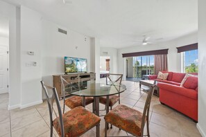 A modern living room with a red sofa, a glass dining table with chairs, a television, and a balcony with a view. - 4403 Spacious 2/2 Resort Condo Near Disney (Orlando)