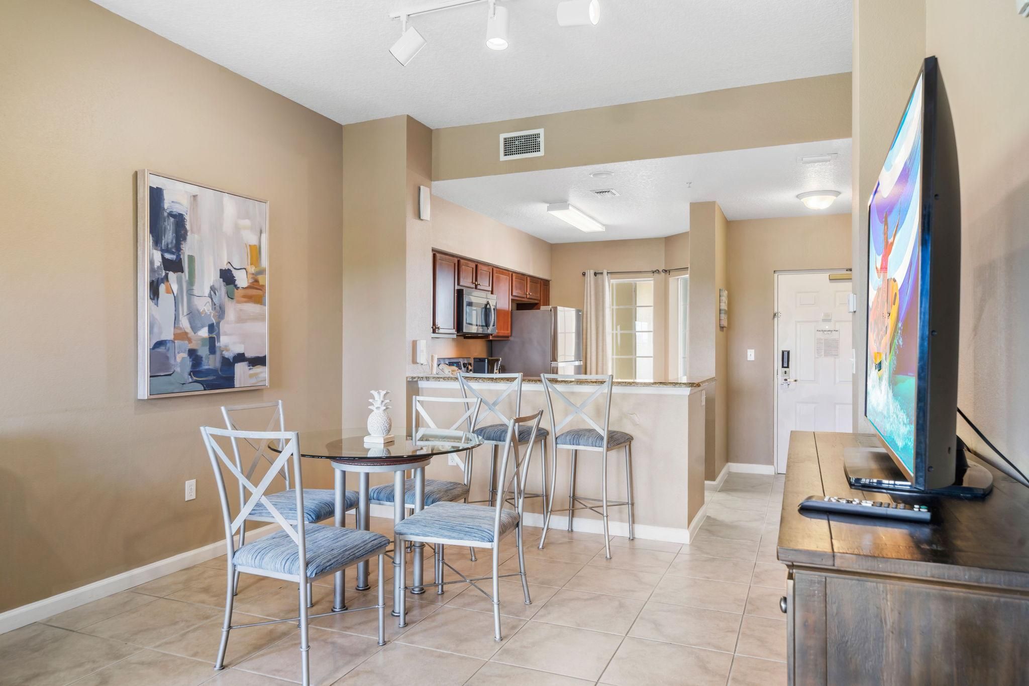 A modern living room with a dining area, kitchen, and a large flat-screen TV.
