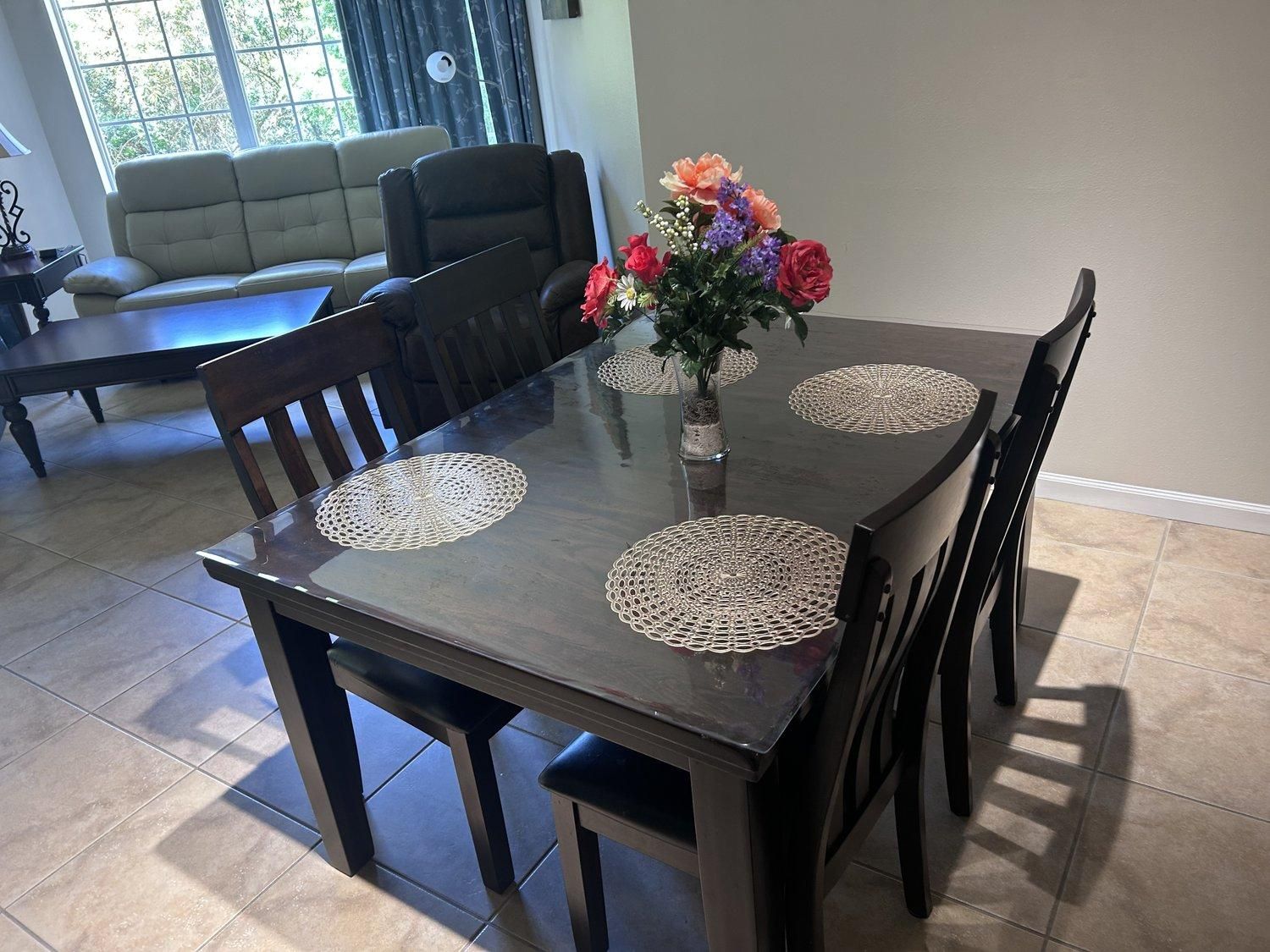 Une table à manger avec quatre chaises, un vase rempli de fleurs et une fenêtre en arrière-plan.