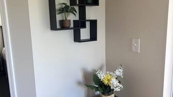 Un coin avec une table marron foncé, une étagère noire fixée au mur où sont posées des plantes en pot, et un vase rempli de fleurs.