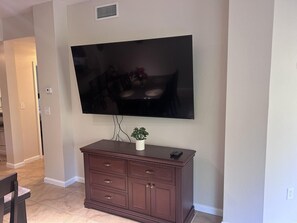 A flat-screen TV mounted on a wall above a dark wooden cabinet with drawers. - 5203 Spacious 2/2 Resort Condo Near Disney (Orlando)