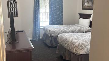 Une chambre d’hôtel avec deux lits, un bureau, une fenêtre avec des rideaux et un luminaire au plafond.