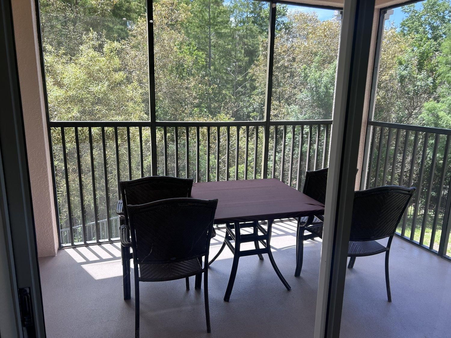 Un balcon avec une table et des chaises, donnant sur une zone boisée.