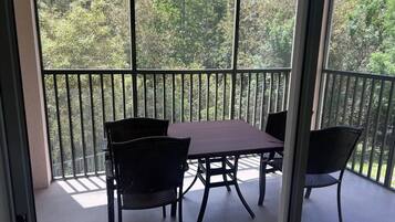 Un balcon avec une table et des chaises, donnant sur une zone boisée.