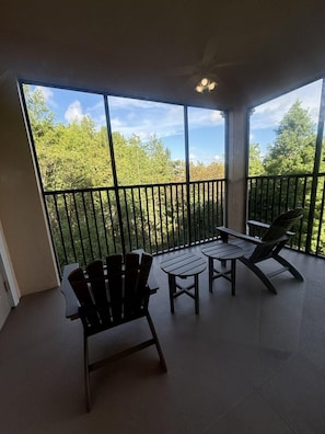 A balcony with two Adirondack chairs and a small table, overlooking a forested area. - 5303 Spacious 2/2 Resort Condo Near Disney (Orlando)