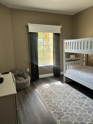 A bedroom with a bunk bed, a desk with a chair, a bean bag chair, and a window with curtains. - 5303 Spacious 2/2 Resort Condo Near Disney (Orlando)