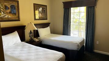 Une chambre d’hôtel avec deux lits simples, une table de chevet avec une lampe, un téléphone et deux tableaux encadrés au mur.