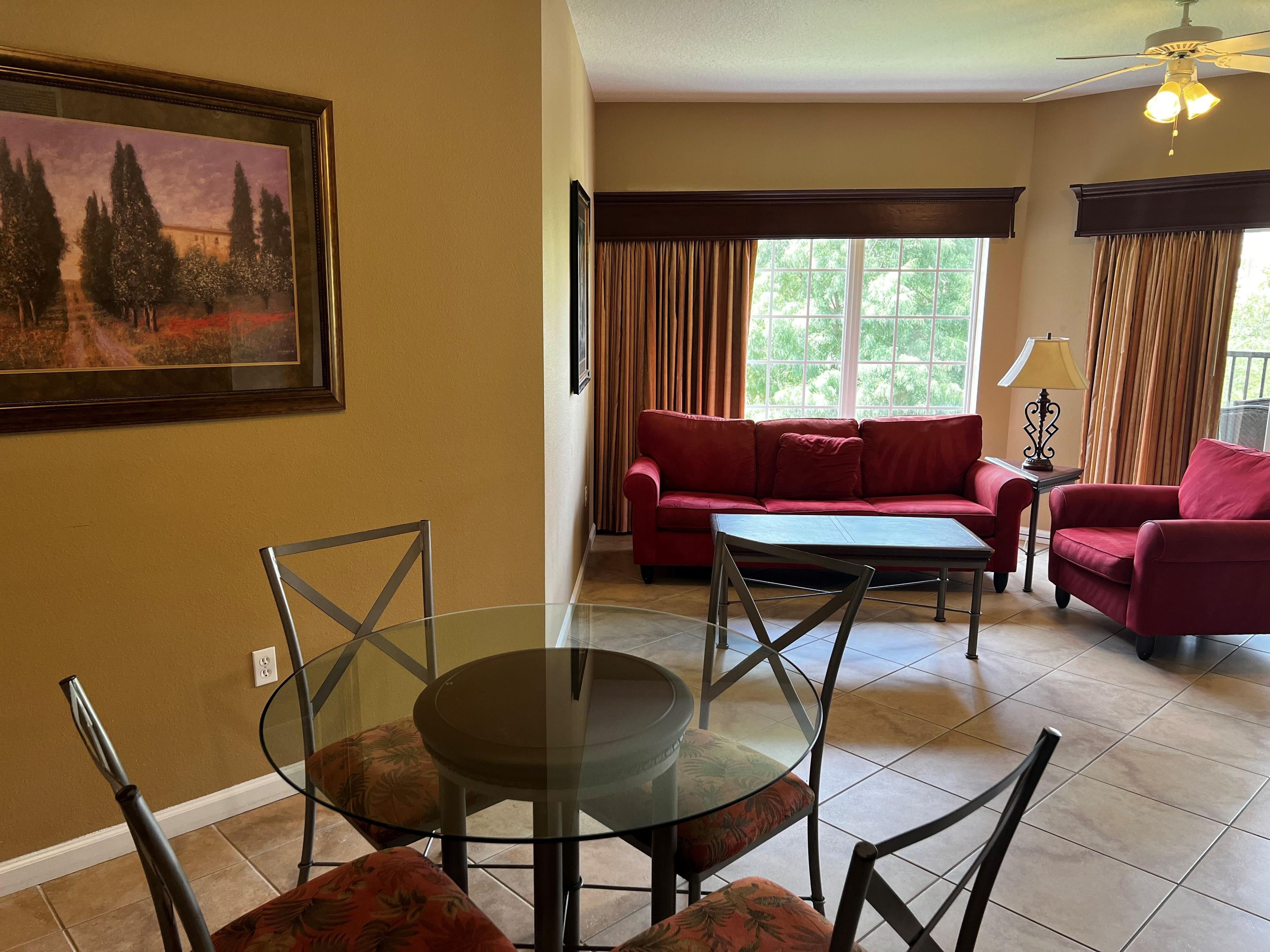 Un salon avec une table en verre, un canapé rouge et un tableau accroché au mur.