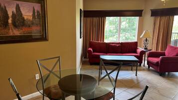Un salon avec une table en verre, un canapé rouge et un tableau accroché au mur.