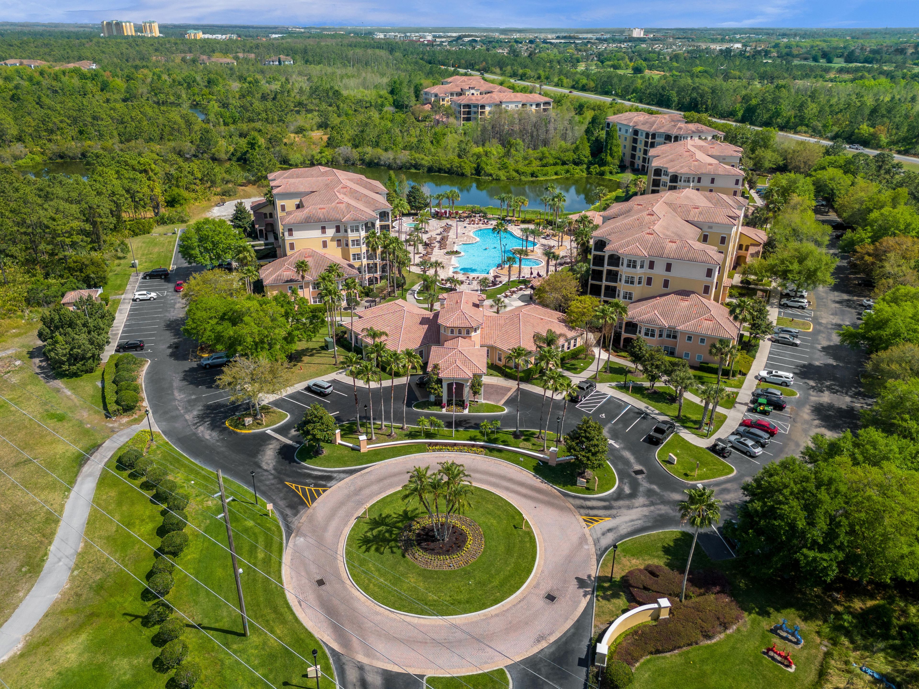 An aerial view of a resort with a central pool, multiple buildings, and a circular driveway.