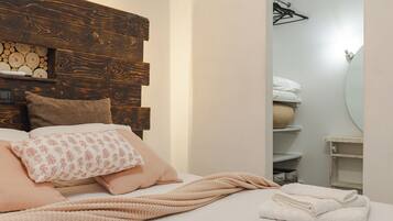 Una camera da letto con una testiera in legno, un letto con numerosi cuscini, una coperta lavorata a maglia e un asciugamano bianco piegato con cura.