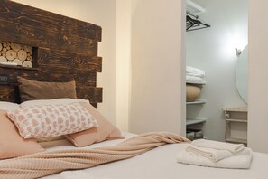 Un dormitorio con cabecera de madera, cama con múltiples almohadas, manta de punto y una toalla blanca doblada con cuidado.