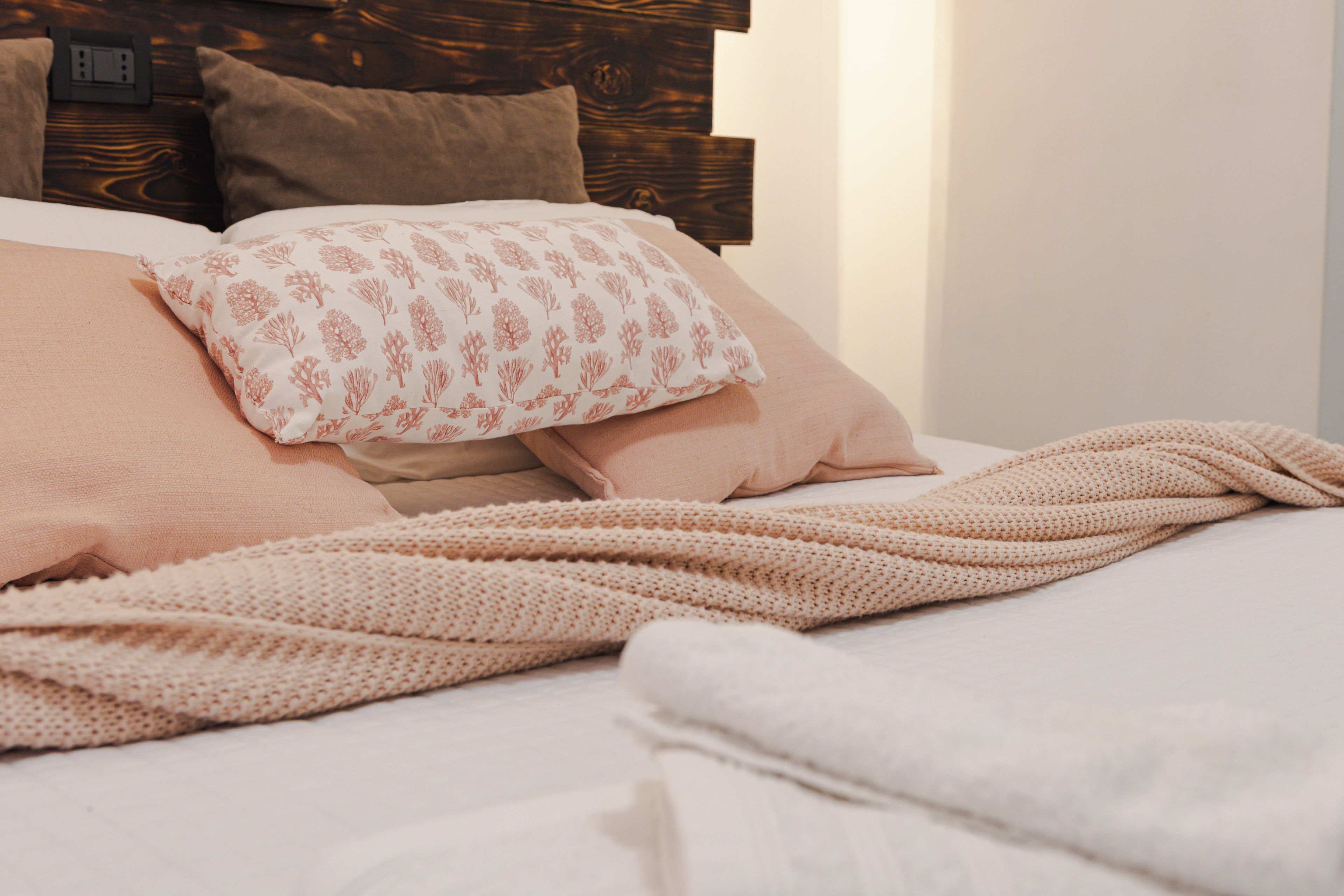 Una cama con una manta tejida, almohadas y un cabecero de madera.