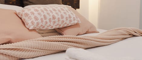 Una cama con una manta tejida, almohadas y un cabecero de madera.