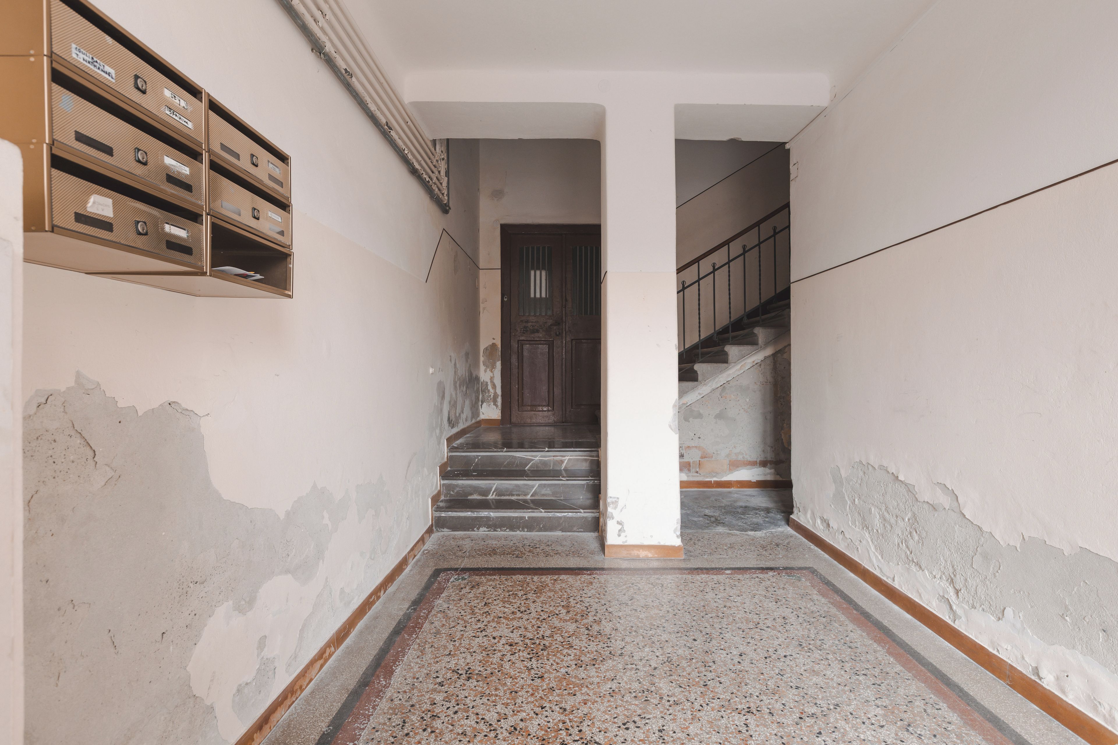 Ein Flur mit einer Treppe, die zu einer Tür führt, einem Briefschlitz in der Wand und einem beschädigten Boden.