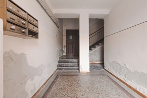 A hallway with a staircase leading to a door, a mail slot on the wall, and a damaged floor. - [Piazza Unità / San Giusto] Suite Apartment + Wi-Fi (Trieste)
