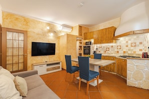 A compact living space with a kitchenette, a dining area with blue chairs, a flat-screen TV, and a sofa. - [Piazza Unità / San Giusto] Suite Apartment + Wi-Fi (Trieste)