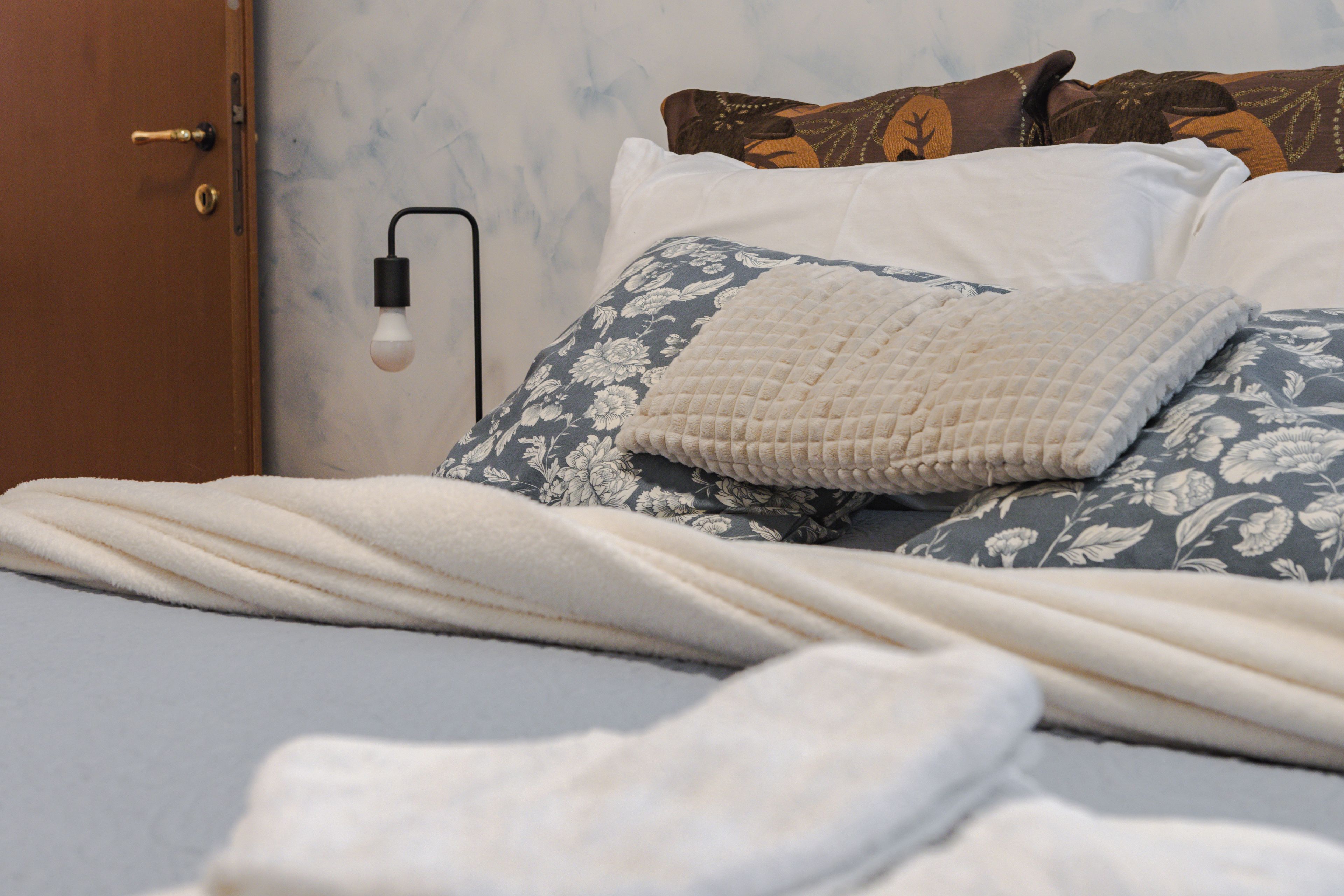A bed with a white blanket, a floral pillow, and a textured pillow.