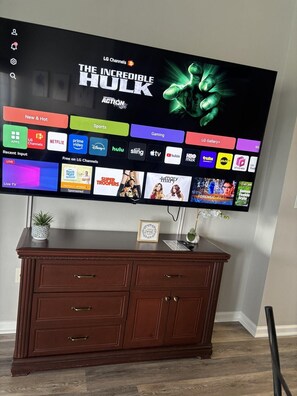 A flat-screen TV mounted on a wall above a wooden dresser with drawers. - 5506 Spacious 2/2 Resort Condo Near Disney (Orlando)