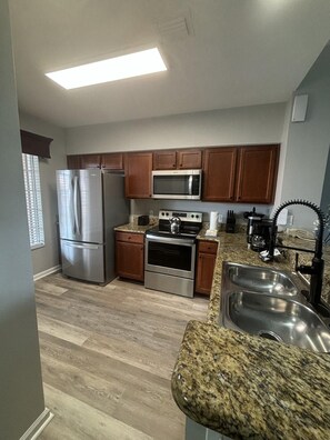 A modern kitchen with stainless steel appliances, wooden cabinets, granite countertops, and a double sink. - 5506 Spacious 2/2 Resort Condo Near Disney (Orlando)