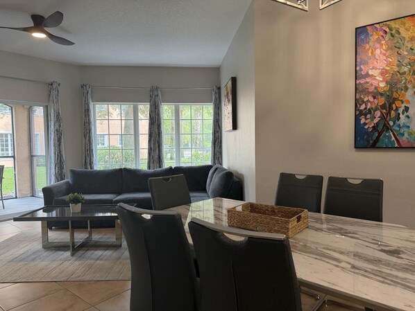 Una sala de estar moderna con un sofá, una mesa de comedor de vidrio y un ventilador de techo.