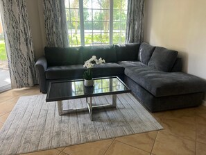 Una sala de estar con un sofá modular, una mesa de centro de vidrio con una planta en maceta, y vistas a través de un amplio ventanal.