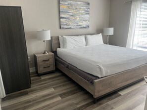Un dormitorio con cama, mesitas de noche, una pintura colgada en la pared y una ventana con persianas.