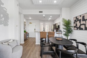 A modern living room with a grey sofa, a dining area with a round table and chairs, and a kitchen in the background. - 6306 Stunning 2/2 Resort Condo Near Disney (Orlando)