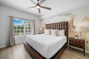 Ein Schlafzimmer mit einem großen Bett, einem Deckenventilator, einem Nachttisch mit Lampe und einem Fenster mit Vorhängen.